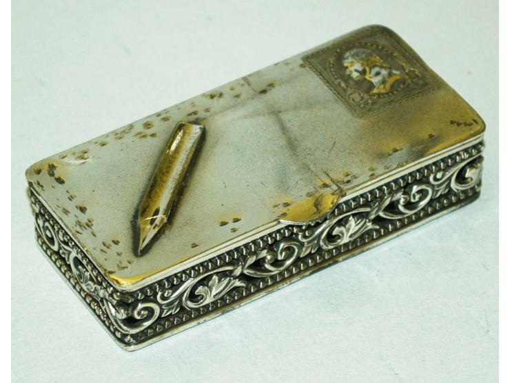 Briefmarkendose aus versilbertem Metal mit getriebenem Bild einer Briefmarke und aufgesetzter Schreibfeder. Die Dose hat zwei