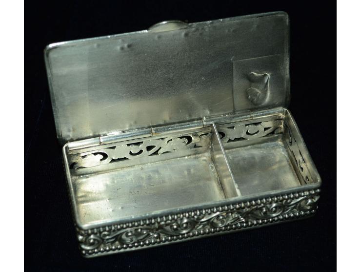 Briefmarkendose aus versilbertem Metal mit getriebenem Bild einer Briefmarke und aufgesetzter Schreibfeder. Die Dose hat zwei